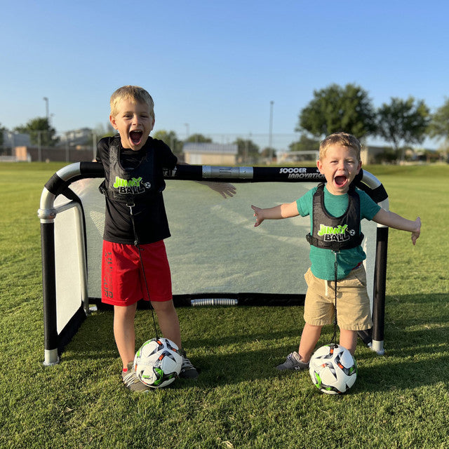 Two young kids smiling and posing with soccer balls in front of a portable Quick Fold Aluminum Soccer Goal on a sunny field