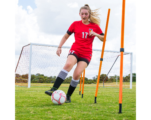 Soccer player dribbling through orange adjustable agility poles on a grass field