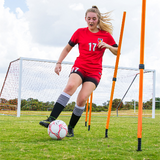 Soccer player dribbling through orange adjustable agility poles on a grass field