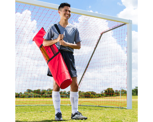 Athlete carrying agility pole set bag on a soccer field in front of a goal