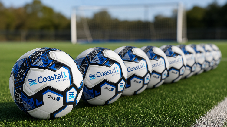 Line of Coastal1 Credit Union custom soccer balls on a turf field with a soccer goal in the background.