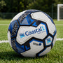 Customized Coastal1 Credit Union soccer ball displayed on a grass field with a soccer goal in the background.