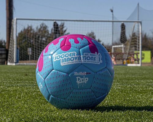 Blue and pink Drip Soccer Ball on turf with a soccer goal blurred in the background
