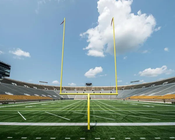 Yellow American football goalposts installed on a stadium football field with bleachers in the background.