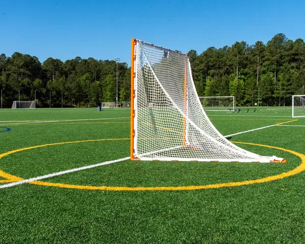 Orange lacrosse goal frame with white netting positioned on a green artificial turf sports field.