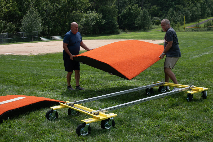 Two people lifting a portable pitching mound near the Mound Taxi transport system