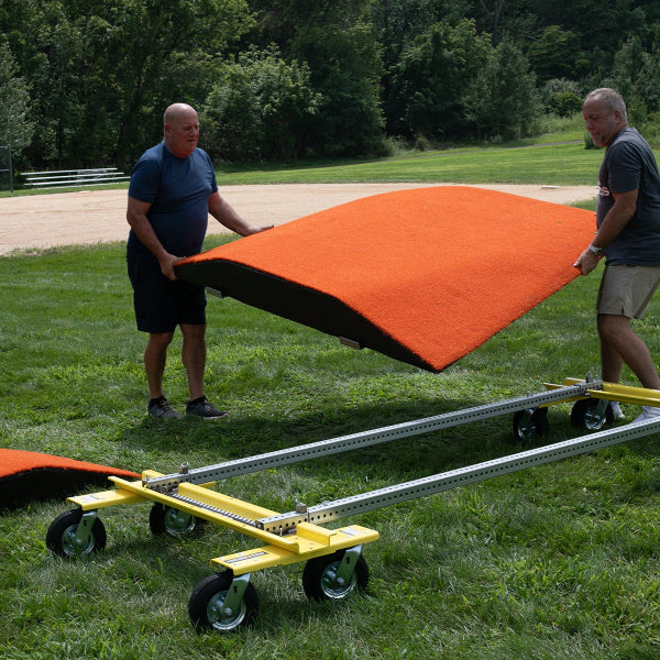Two people lifting a portable pitching mound near the Mound Taxi transport system