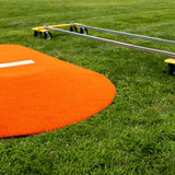 Portable pitching mound next to assembled Mound Taxi system on grass field