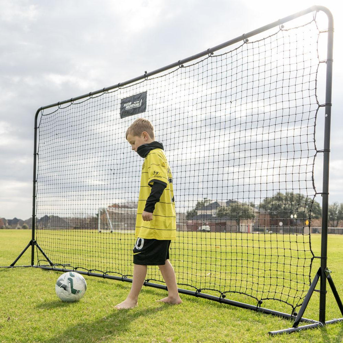 Child in a yellow sports outfit standing next to a large soccer net on a grass field.