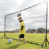 Child in a yellow sports outfit standing next to a large soccer net on a grass field.
