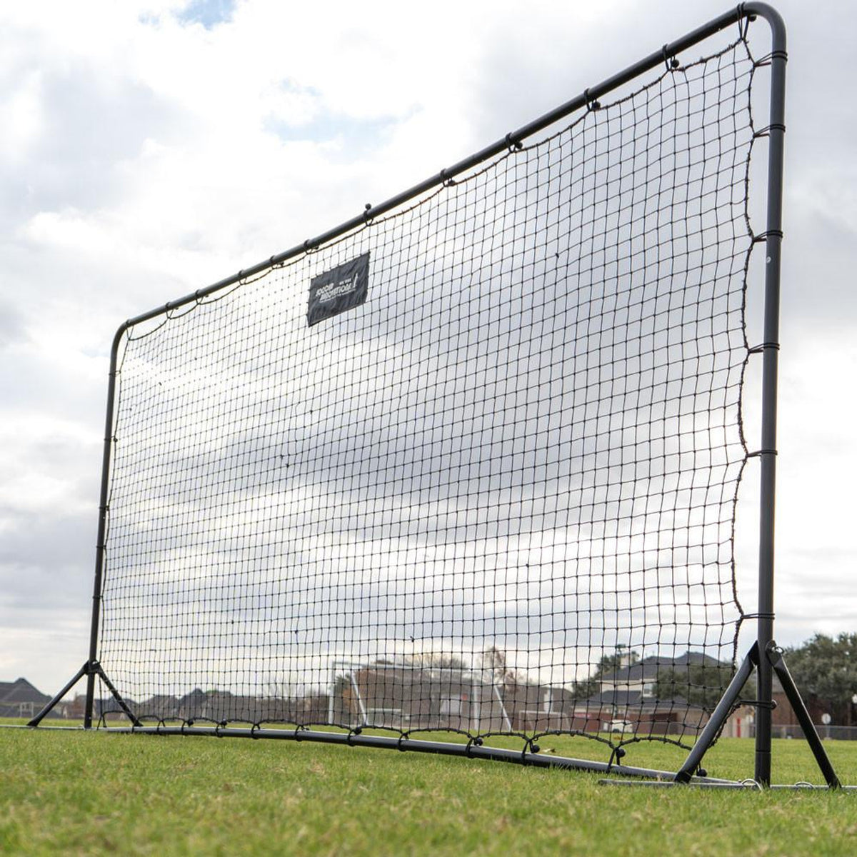 Large black sports net on a grassy field with a cloudy sky.