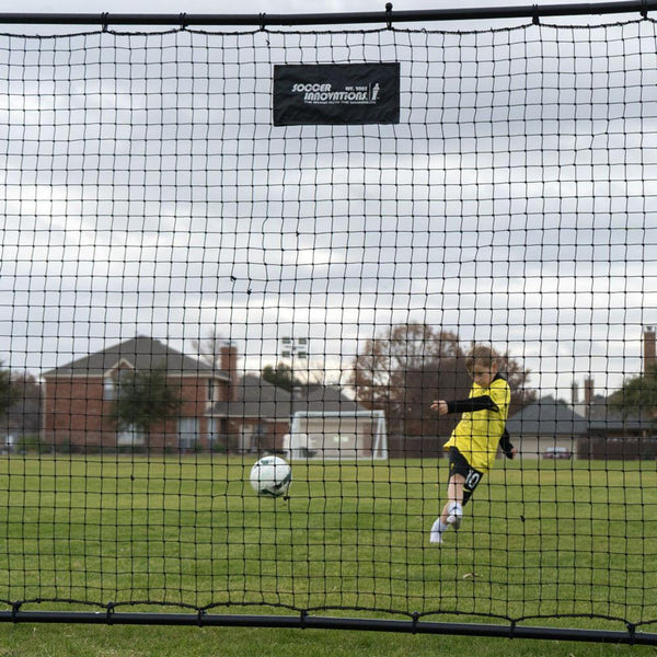 Person playing soccer on a field with a goal net in the foreground