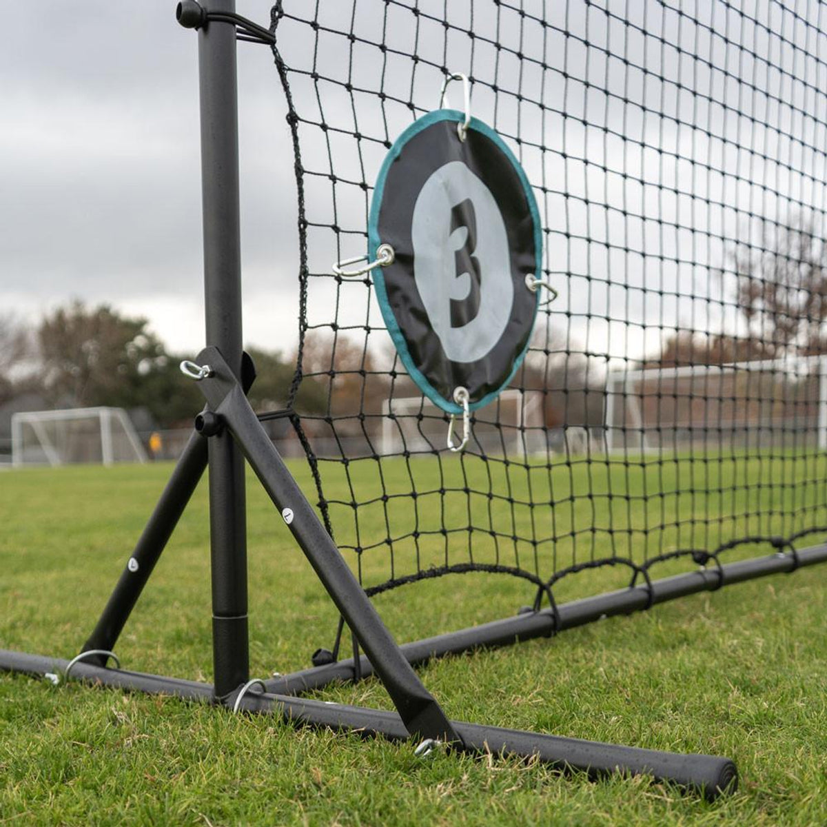 Goalie training device with a brand logo attached to a soccer net on a grass field.