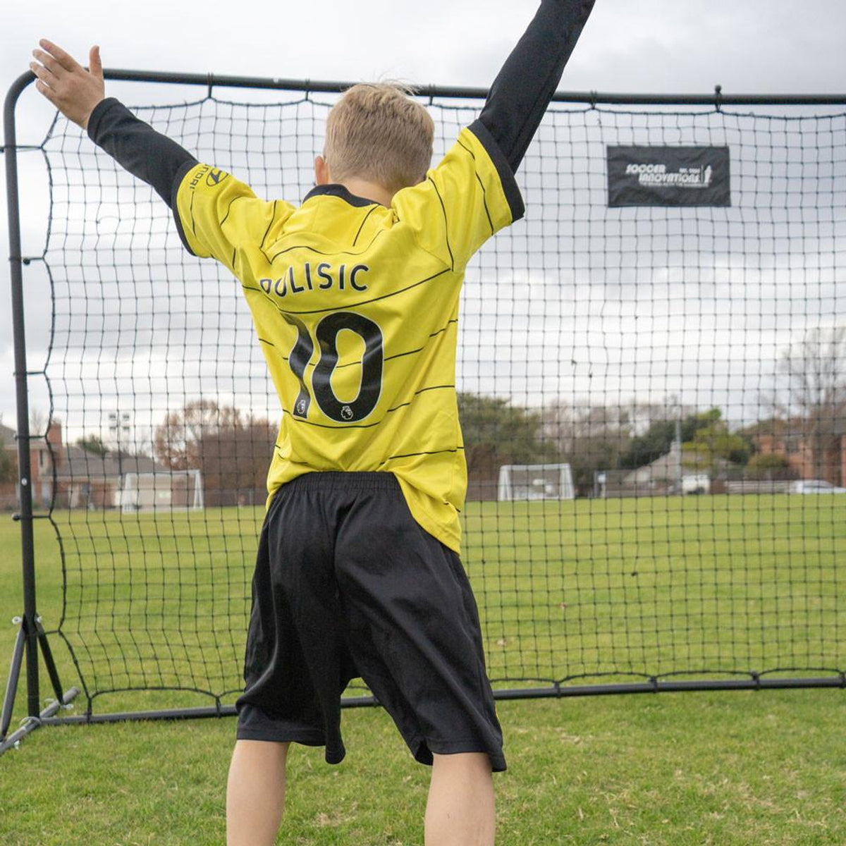 Child in a yellow soccer jersey with 'Gulisic' and number '10' standing in front of a soccer goal.