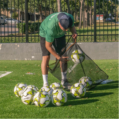 Close-up of black mesh soccer ball bag holding multiple white and neon yellow soccer balls on turf